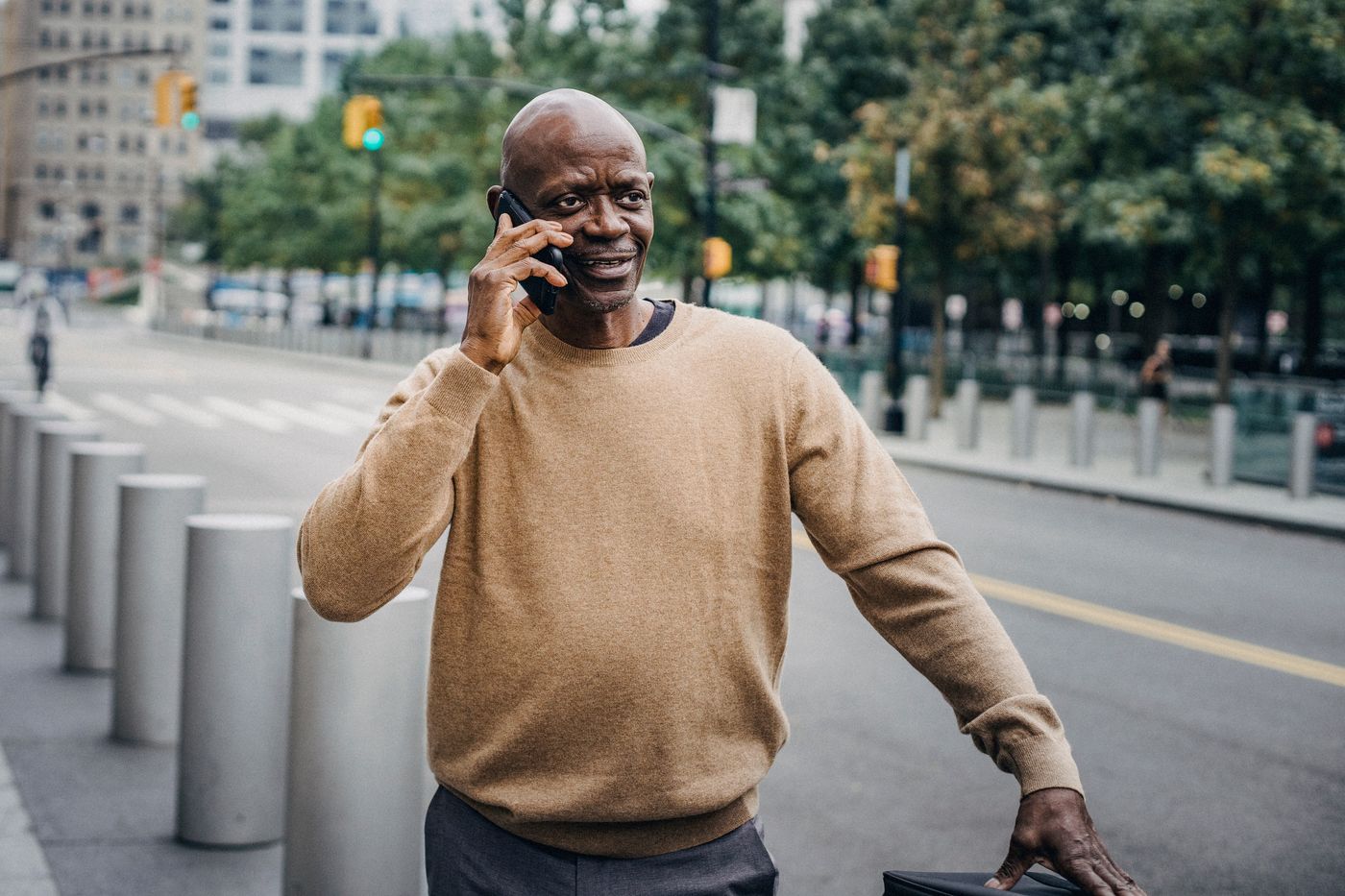 A professional in warm-toned everyday clothing on a phone call outside on a city street mid-workday, illustrating how an employee might reach chaplain support through CALLACHAP.